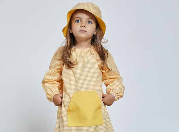 Menina vestida com uma das Batas escolares fabricadas pela Unifardas na cor amarela com quadrados brancos