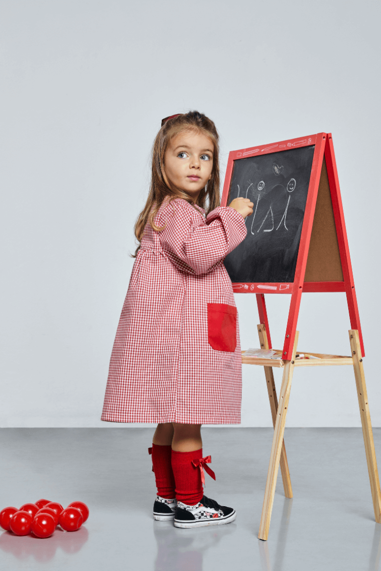 Menina vestida com uma bata escolar infantil de cor vermelha fabricada pela unifardas