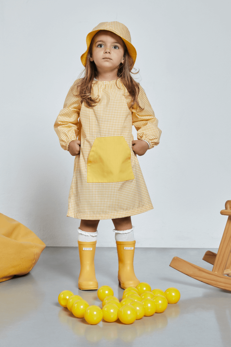 Menina vestida com uma bata para infantário de cor amarela para uniforme escolar