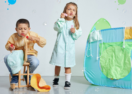 Crianças vestidas com uma bata verde e outra amarela para serem usadas como vestuário escolar fabricadas pela Unifardas