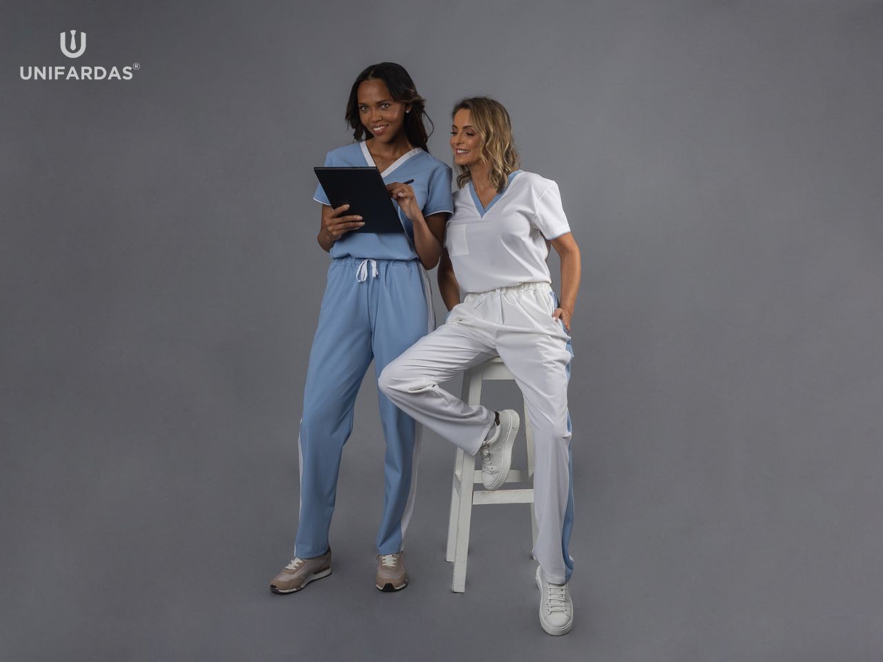 Capa do artigo de blog da Unifardas com o título o que são pijamas cirúrgicos. Neste capa estão duas profissionais de saúde vestidas com um pijama cirúrgico branco e outro branco.